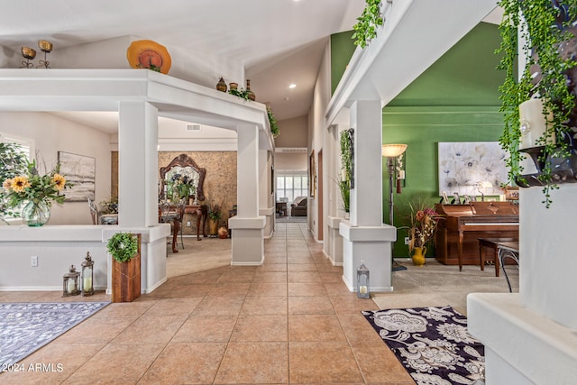 entryway with vaulted ceiling, light tile patterned floors, a healthy amount of sunlight, and ornate columns