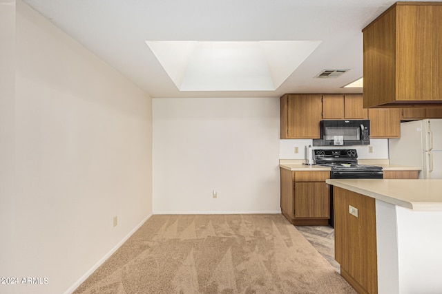 kitchen with light carpet, a tray ceiling, black appliances, and a skylight