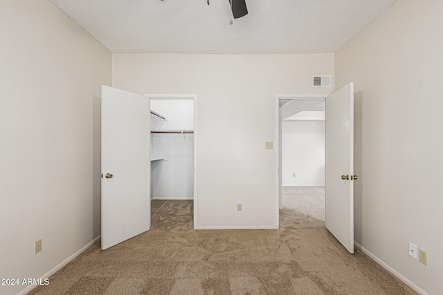 unfurnished bedroom with a closet, a walk in closet, light colored carpet, a textured ceiling, and ceiling fan