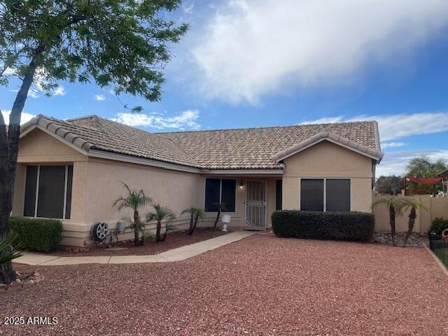 ranch-style house with a tiled roof, fence, and stucco siding