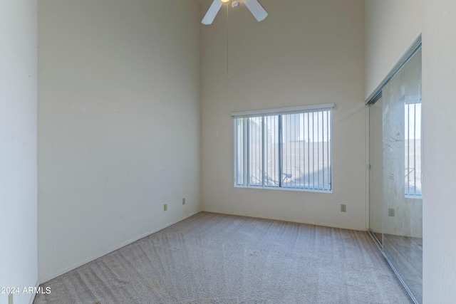 carpeted empty room featuring ceiling fan, plenty of natural light, and a high ceiling