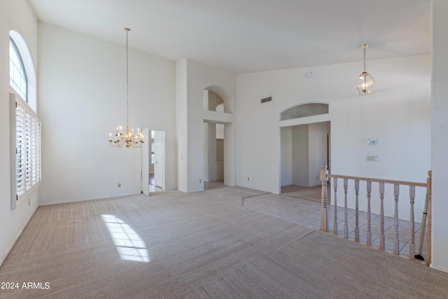 carpeted empty room featuring an inviting chandelier and high vaulted ceiling