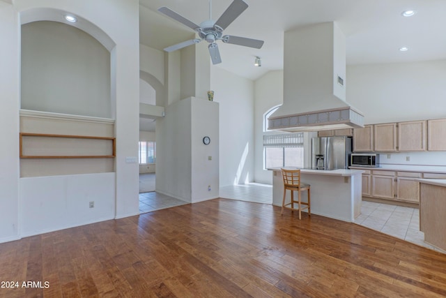 kitchen with a center island, a kitchen bar, light brown cabinetry, custom range hood, and appliances with stainless steel finishes