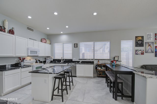 kitchen featuring white cabinetry, a kitchen island, a breakfast bar area, and white appliances