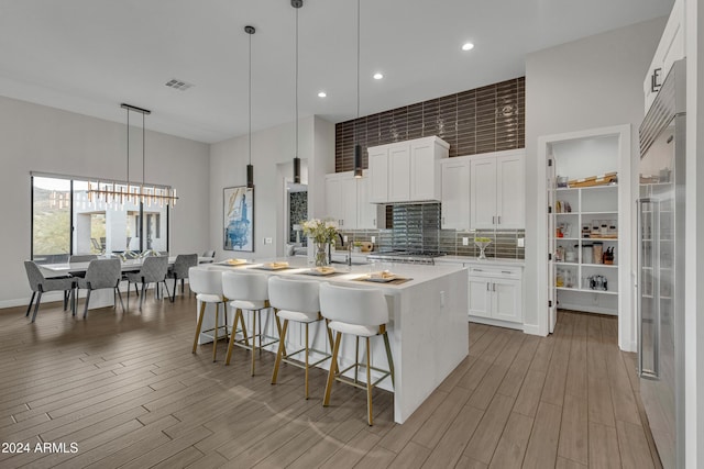 kitchen featuring a kitchen breakfast bar, light hardwood / wood-style flooring, decorative light fixtures, a kitchen island with sink, and white cabinets