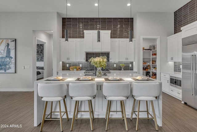 kitchen featuring hardwood / wood-style floors, white cabinets, a center island with sink, appliances with stainless steel finishes, and tasteful backsplash