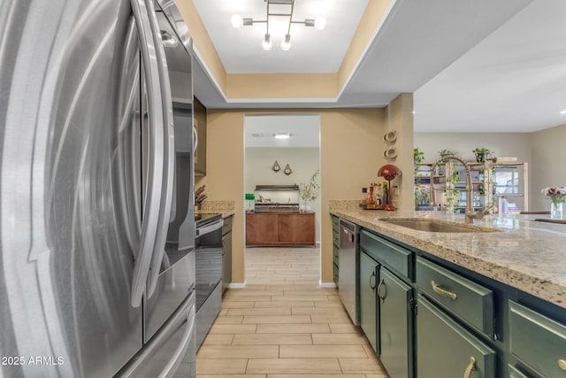 kitchen with stainless steel appliances, light stone counters, green cabinets, and sink