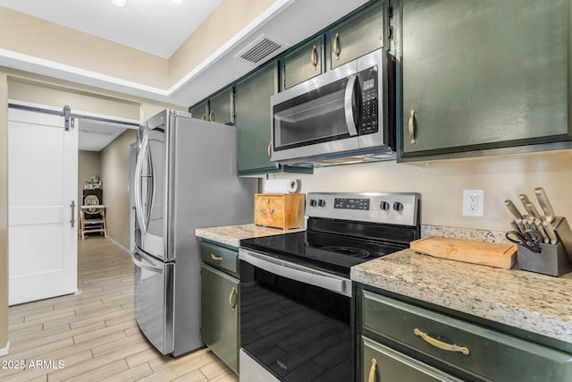 kitchen featuring light stone countertops, appliances with stainless steel finishes, light wood-type flooring, a barn door, and green cabinets