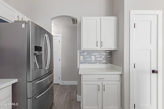 kitchen with stainless steel fridge, backsplash, white cabinetry, and wood-type flooring