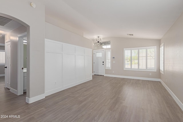 unfurnished living room with hardwood / wood-style floors, lofted ceiling, and a notable chandelier