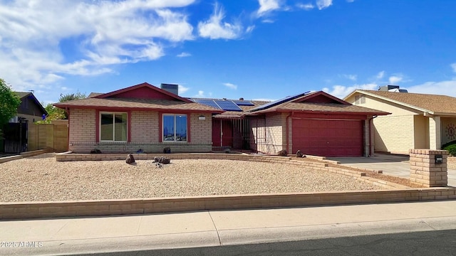 single story home featuring roof mounted solar panels, brick siding, driveway, and an attached garage