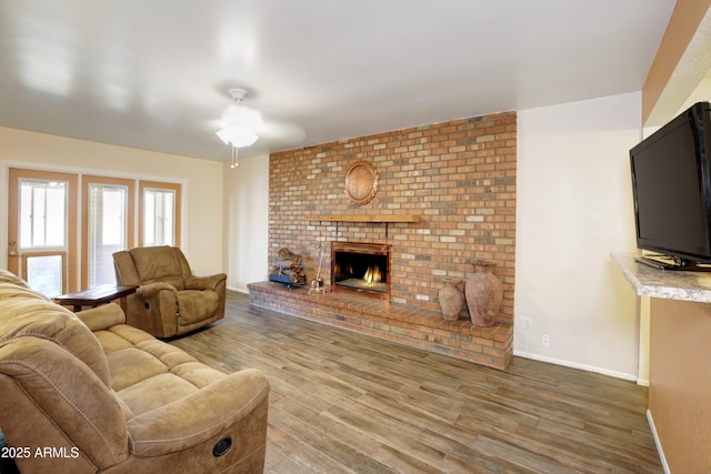 living room featuring a ceiling fan, a fireplace, baseboards, and wood finished floors