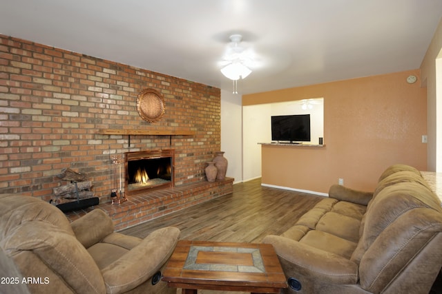 living area with ceiling fan, a brick fireplace, wood finished floors, and baseboards