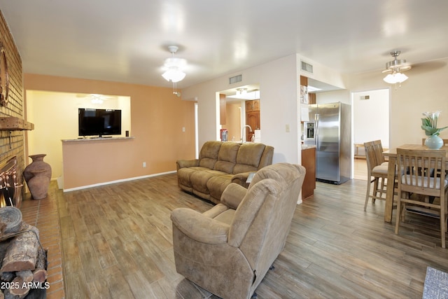 living area featuring a fireplace, visible vents, a ceiling fan, and wood finished floors