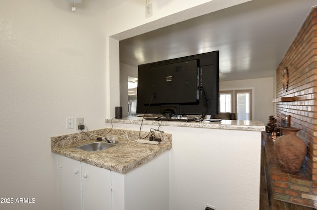 kitchen featuring a peninsula, brick wall, light countertops, and a sink