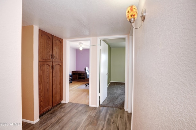 hall with a textured wall, a textured ceiling, baseboards, and wood finished floors