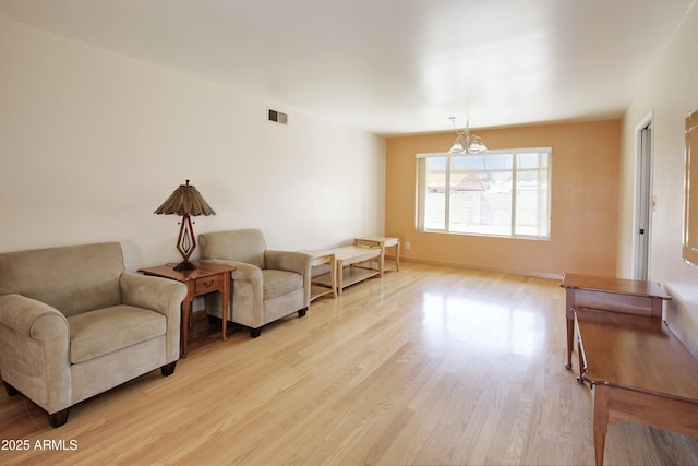 living area with a notable chandelier, light wood finished floors, visible vents, and baseboards