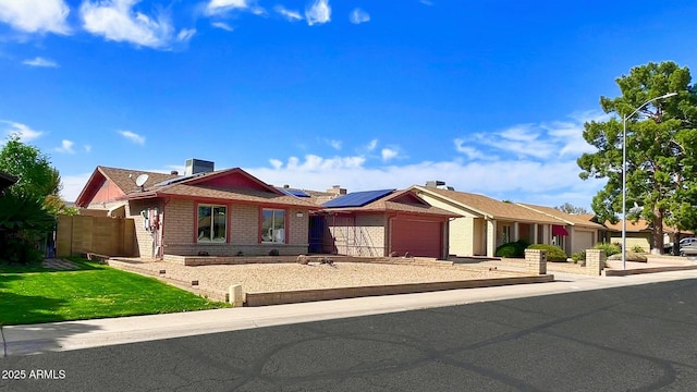 ranch-style house featuring brick siding, an attached garage, a front yard, roof mounted solar panels, and driveway