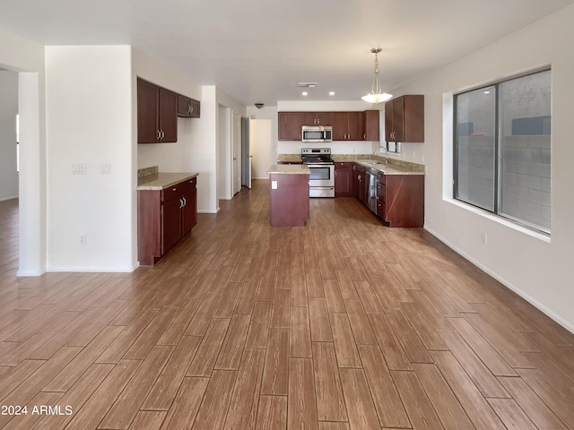 kitchen with a kitchen island, baseboards, wood tiled floor, appliances with stainless steel finishes, and a sink