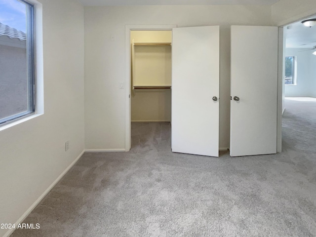 unfurnished bedroom featuring a walk in closet, multiple windows, carpet, and baseboards