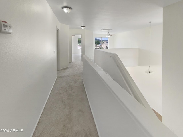 corridor featuring baseboards, an upstairs landing, and light carpet