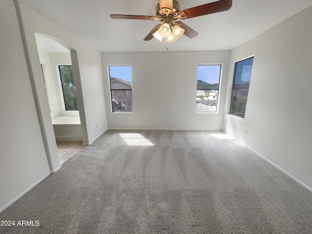 unfurnished bedroom featuring arched walkways, multiple windows, ensuite bath, and carpet