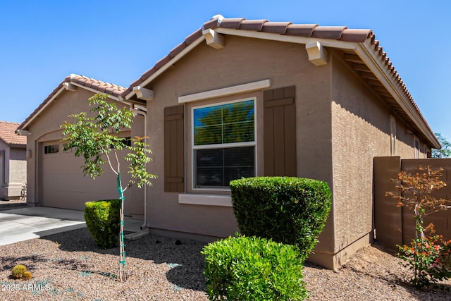 view of side of property with an attached garage, stucco siding, and a tile roof