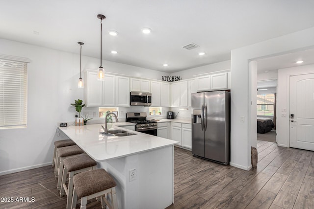 kitchen with visible vents, wood finished floors, a sink, a peninsula, and stainless steel appliances