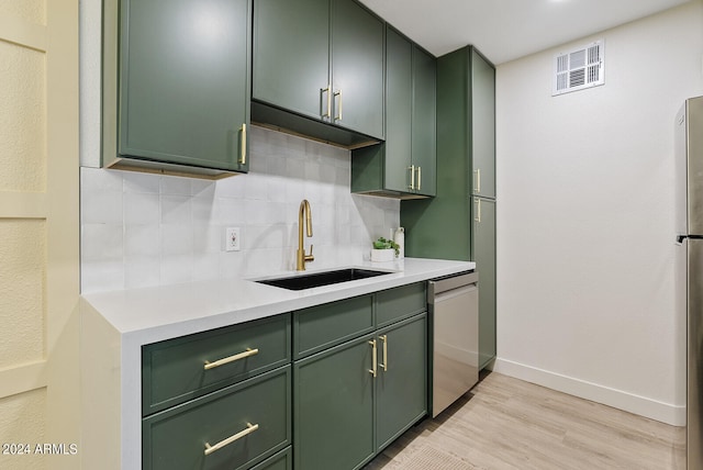 kitchen featuring backsplash, dishwasher, sink, light wood-type flooring, and green cabinetry