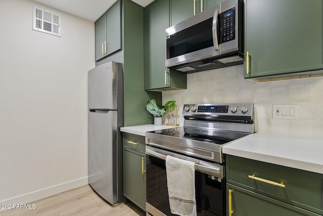 kitchen featuring light wood-type flooring, stainless steel appliances, tasteful backsplash, and green cabinetry