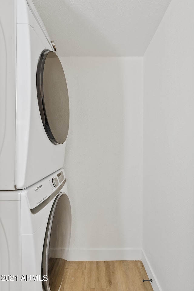 laundry area with light hardwood / wood-style flooring and stacked washer and clothes dryer