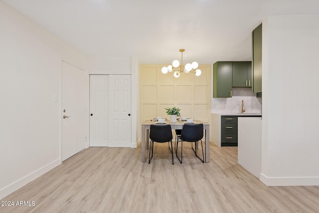 kitchen with green cabinets, light hardwood / wood-style floors, a notable chandelier, and tasteful backsplash