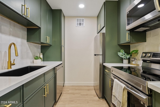 kitchen with stainless steel appliances, light hardwood / wood-style flooring, green cabinets, and tasteful backsplash