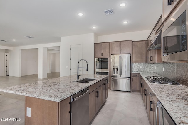 kitchen featuring appliances with stainless steel finishes, sink, light stone counters, and an island with sink