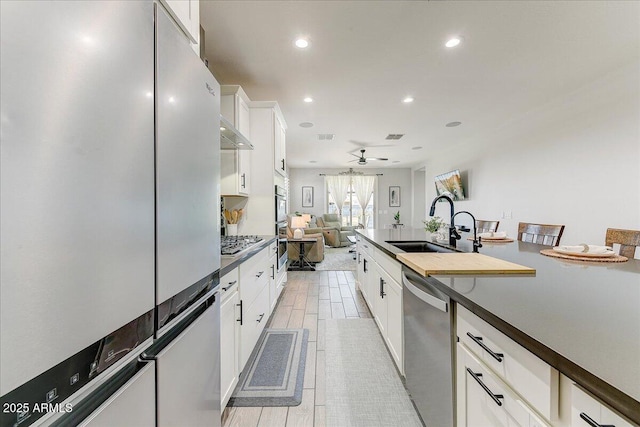 kitchen with dark countertops, open floor plan, stainless steel appliances, white cabinetry, and a sink