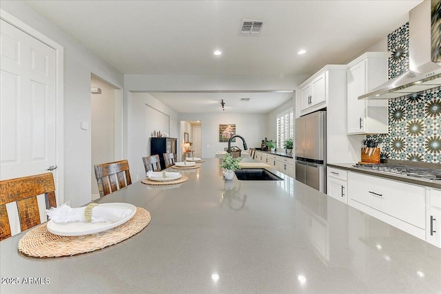 kitchen featuring visible vents, a sink, white cabinetry, appliances with stainless steel finishes, and wall chimney exhaust hood