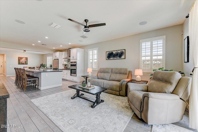 living area with baseboards, a ceiling fan, visible vents, and light wood-type flooring