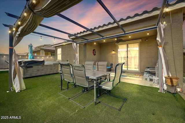 view of patio featuring glass enclosure, outdoor dining space, a ceiling fan, and a hot tub