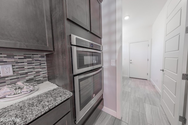 15248 S 182nd Ln, Goodyear, AZ 85338 - kitchen with double oven, backsplash, baseboards, dark brown cabinets, and light stone counters