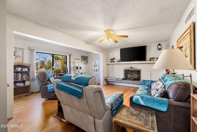 living room featuring ceiling fan, hardwood / wood-style floors, a textured ceiling, and a fireplace