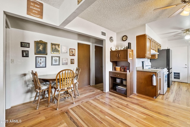 kitchen with ceiling fan, white gas range, light wood-type flooring, and a textured ceiling