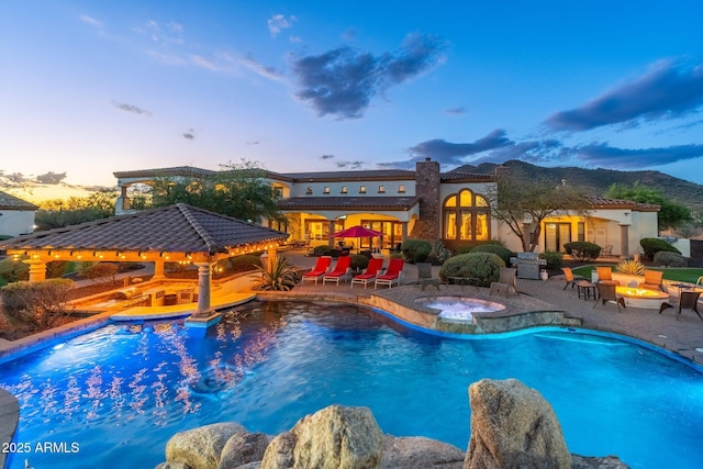 pool at dusk with an outdoor fire pit, a gazebo, area for grilling, an in ground hot tub, and a patio