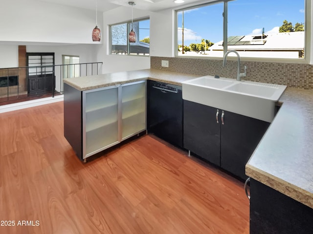 kitchen featuring sink, light hardwood / wood-style flooring, black dishwasher, decorative light fixtures, and kitchen peninsula