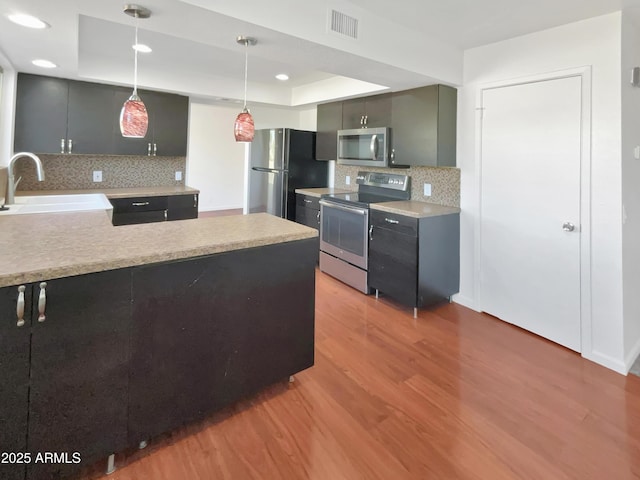 kitchen with tasteful backsplash, stainless steel appliances, a tray ceiling, sink, and pendant lighting