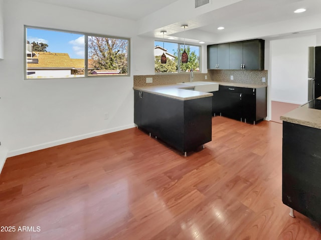 kitchen with pendant lighting, sink, decorative backsplash, light wood-type flooring, and stainless steel refrigerator