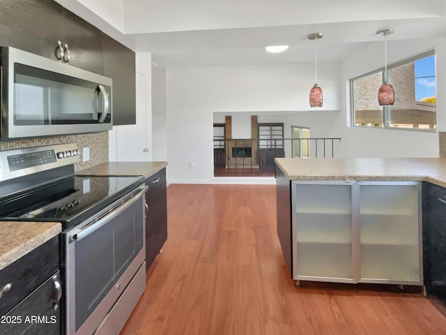 kitchen with backsplash, hanging light fixtures, stainless steel appliances, and light wood-type flooring