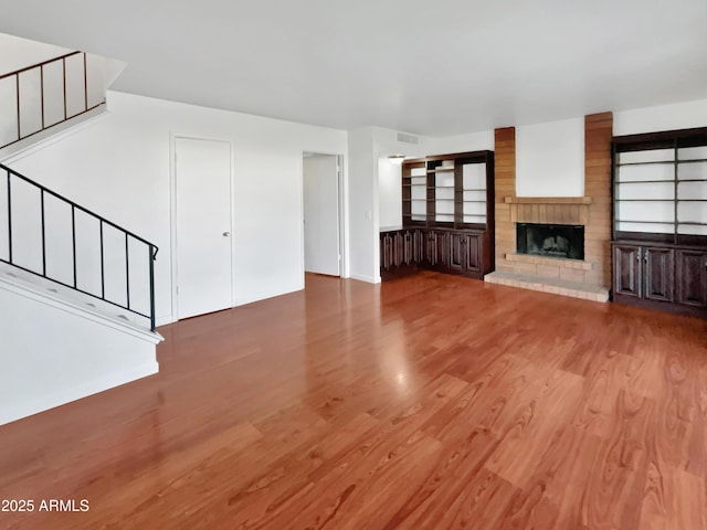 unfurnished living room with built in shelves, wood-type flooring, and a brick fireplace