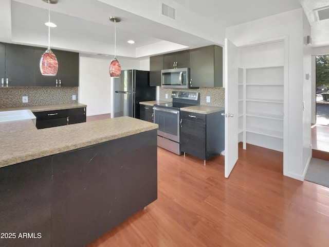 kitchen with pendant lighting, backsplash, a raised ceiling, light wood-type flooring, and stainless steel appliances