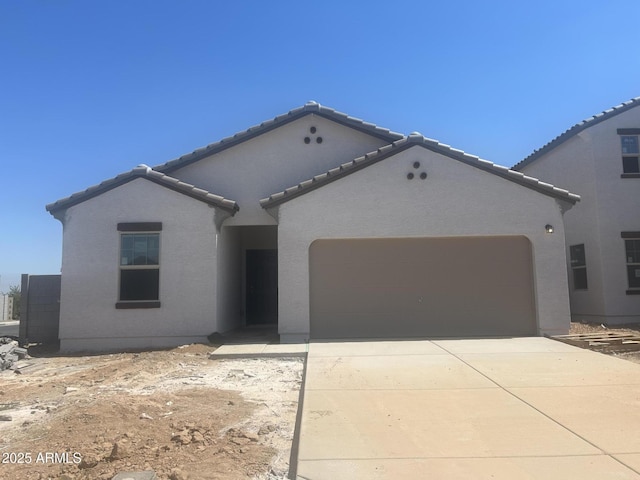 mediterranean / spanish house featuring stucco siding, driveway, a tile roof, and a garage