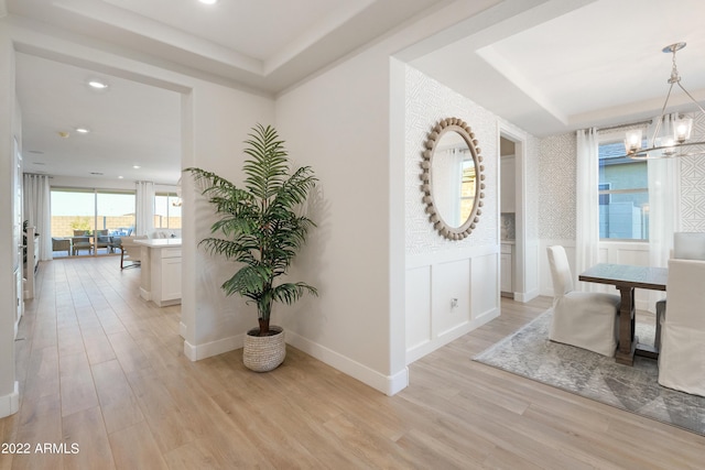 hall featuring a raised ceiling, light hardwood / wood-style floors, and a notable chandelier